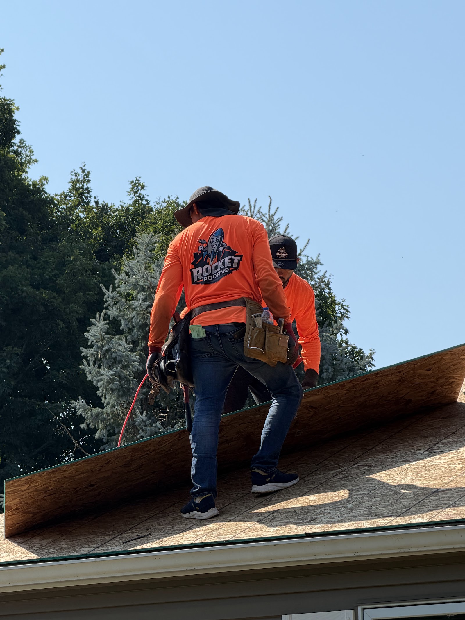 Two Rocket Roofing crew members walking the ridge on bare decking mid-replacement