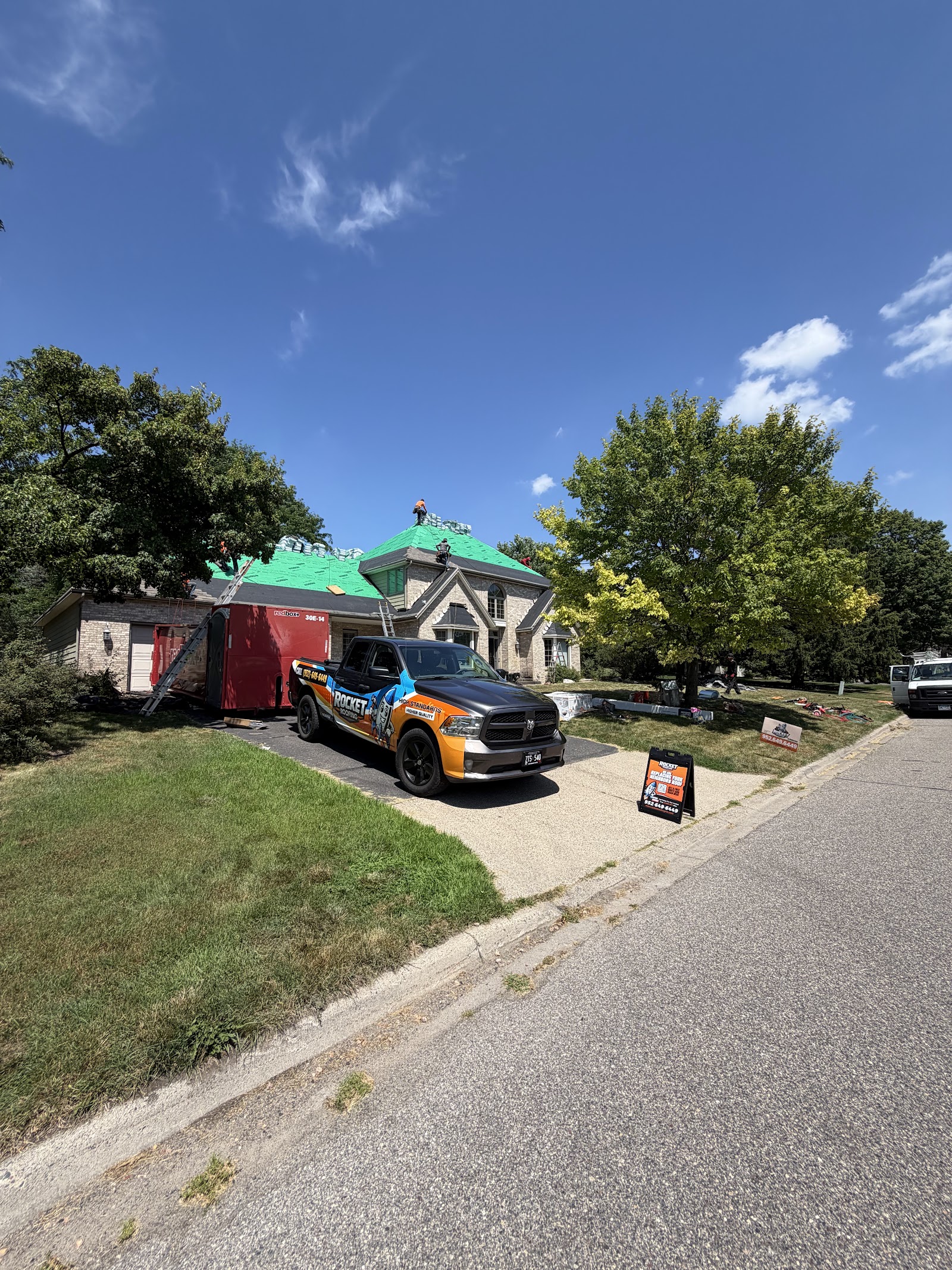 Rocket Roofing truck and yard sign in the driveway with fresh underlayment down on a stone-front home
