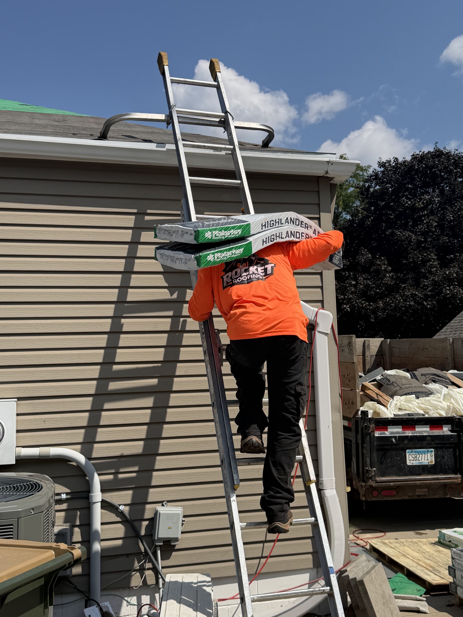 Crew member carrying shingle bundles up a ladder to the roof