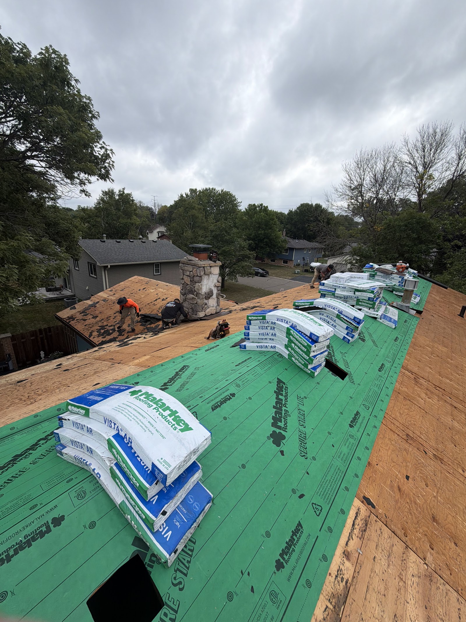 Shingle bundles staged along the ridge over fresh synthetic underlayment on an overcast day
