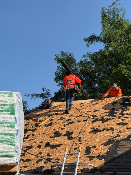 Crew stripping old shingles down to bare roof decking on a sunny Minnesota day